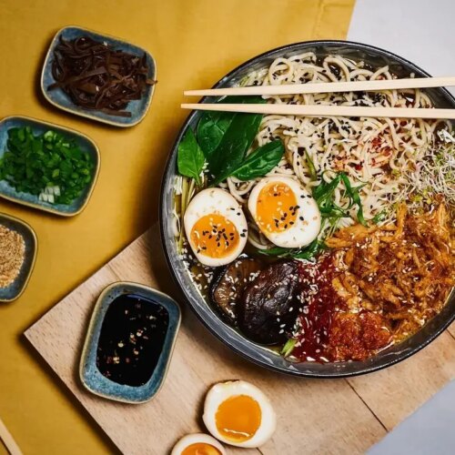 Ramen bowl with meat, egg, sesame seeds, and greens.