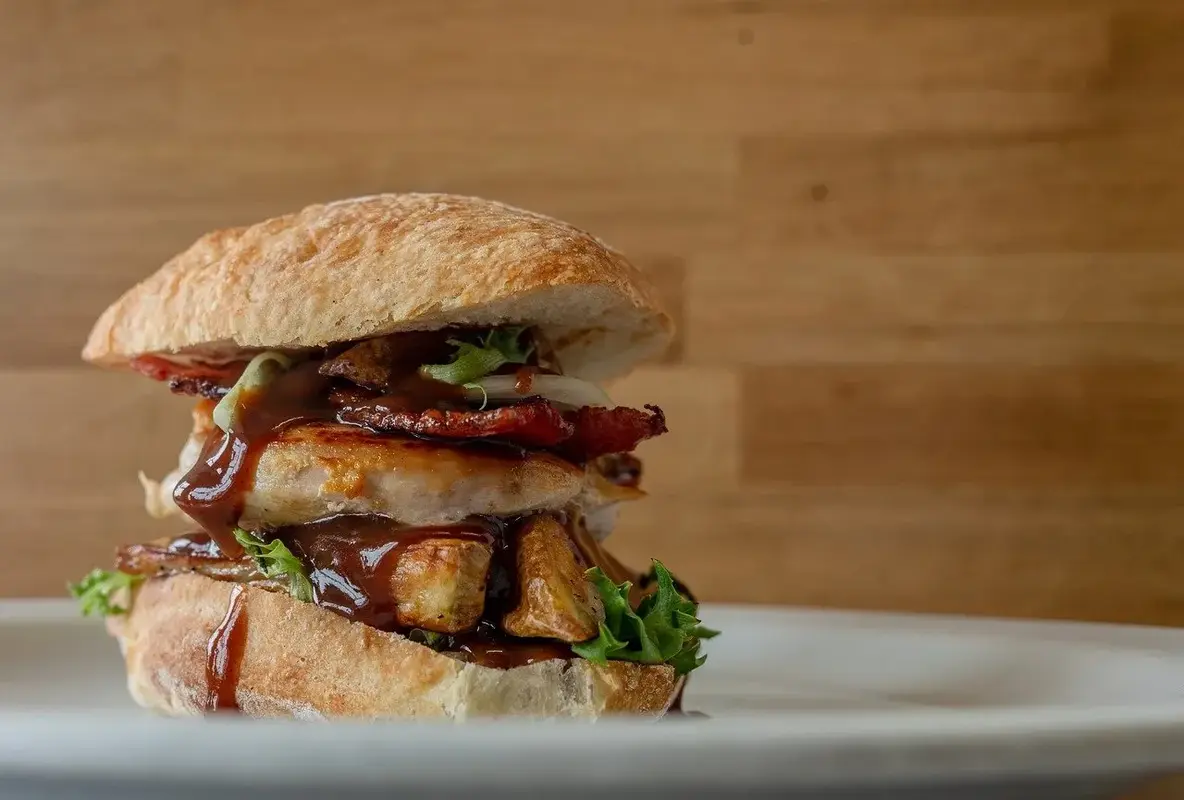 Gourmet ramen burger with chicken, bacon, and arugula on a wooden table.