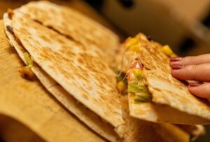 Quesadilla with cranberries, mango, and cheese on wooden board.