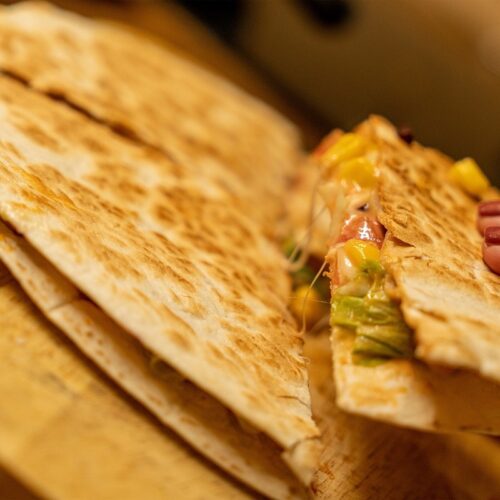 Quesadilla with cranberries, mango, and cheese on wooden board.